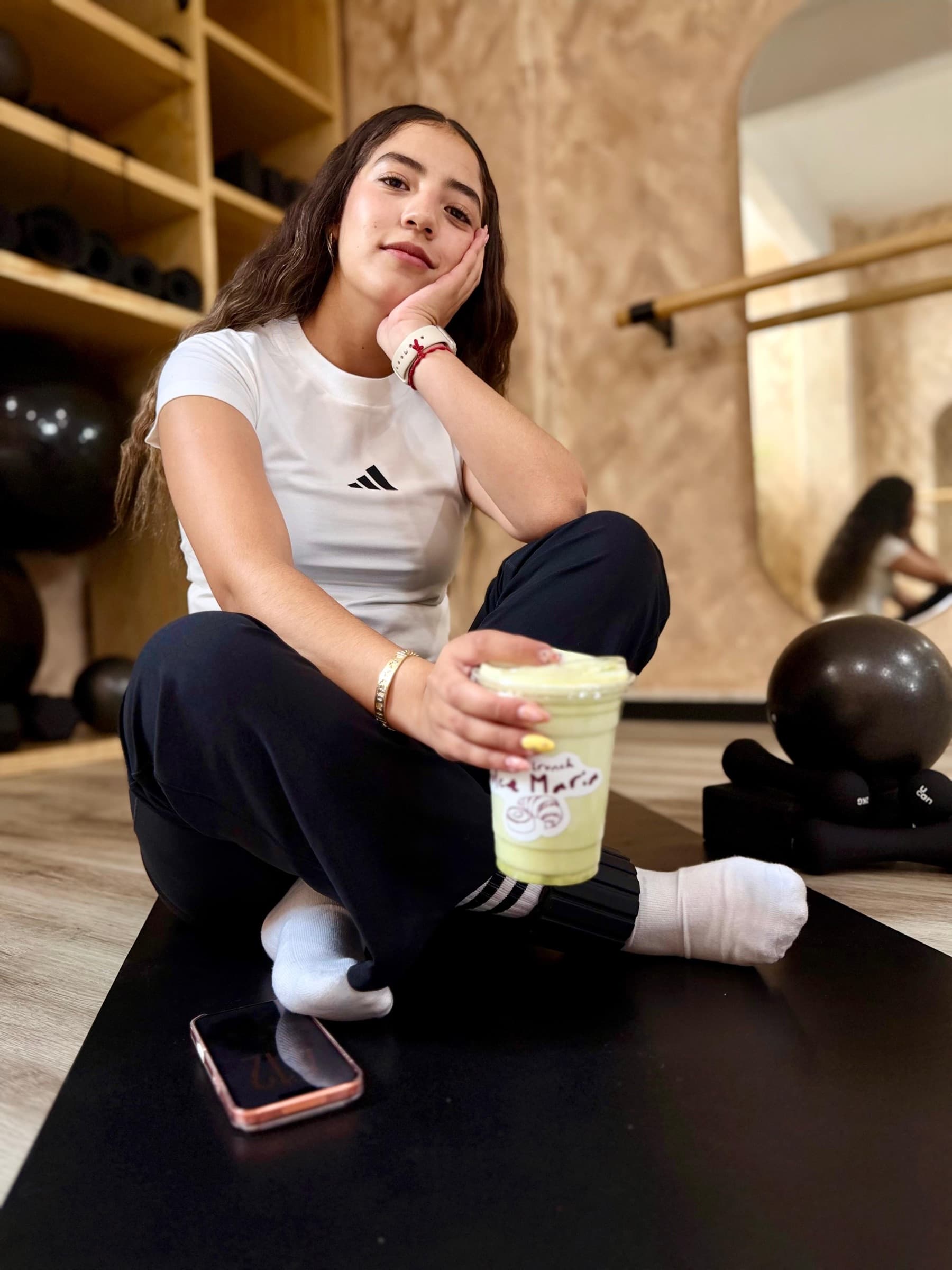 Alumna de YW Studio descansando sobre el tapete con un smoothie después de clase